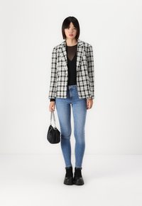 Black and white checked blazer over a black top, blue skinny jeans, black ankle boots, and a small black handbag with a chain handle.
