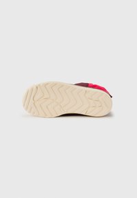 Såle av en sko med en teksturert beige yttersåle med et zigzag-mønster, kontrasterende burgunder øvre materiale og en rosa detalj.