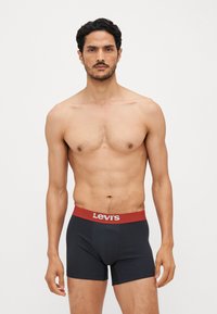 Boxers en coton noirs avec une ceinture rouge arborant le logo "Levi's". Le design comprend une coupe ajustée et une texture lisse.