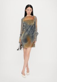 Metallisches Kleid mit plissierter Textur in einem Farbverlauf aus Grün, Orange und Blau, mit langen Ärmeln und hohem Ausschnitt. Silbrige Clutch.