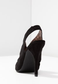 Scarpa alta in suede nera con punta affusolata, apertura sul retro e fodera interna a stampa leopardata. Presenta un sottile tacco a stiletto.