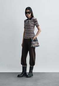 Wielokolorowa dzianinowa koszulka polo z czarnym kołnierzykiem, w zestawie z brązowymi spodniami w wzór zygzak. Czarne botki do kolan oraz torebka w wzór.