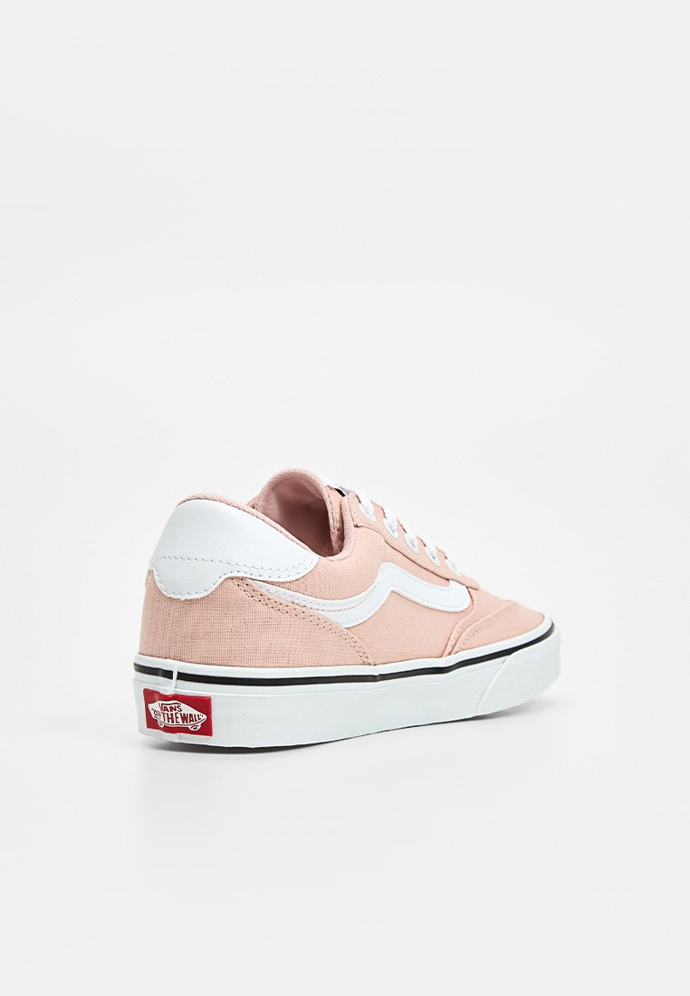 Zapatillas de lona rosa claro con acentos blancos, diseño de cordones, suela negra y logo de Vans en el talón. Forma redondeada y tejido texturizado.