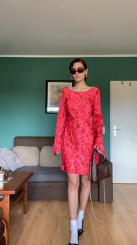 Červené květinové šaty s dlouhými rukávy a výstřihem ve tvaru lodi. Nosené s bílými ponožkami a černými botami, doplněné hnědou kabelkou a slunečními brýlemi.