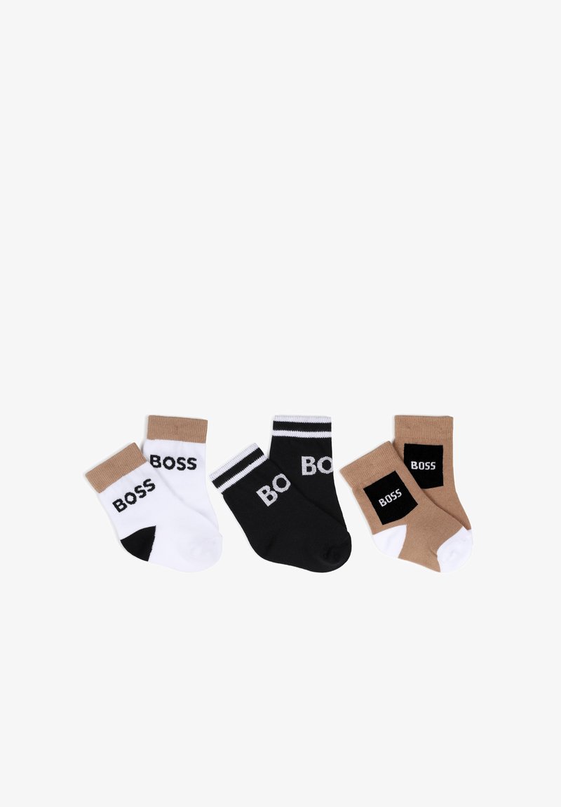 Trois paires de chaussettes basses en blanc, noir et beige, chacune arborant le mot « BOSS » sur le bord ou le côté, disposées côte à côte.