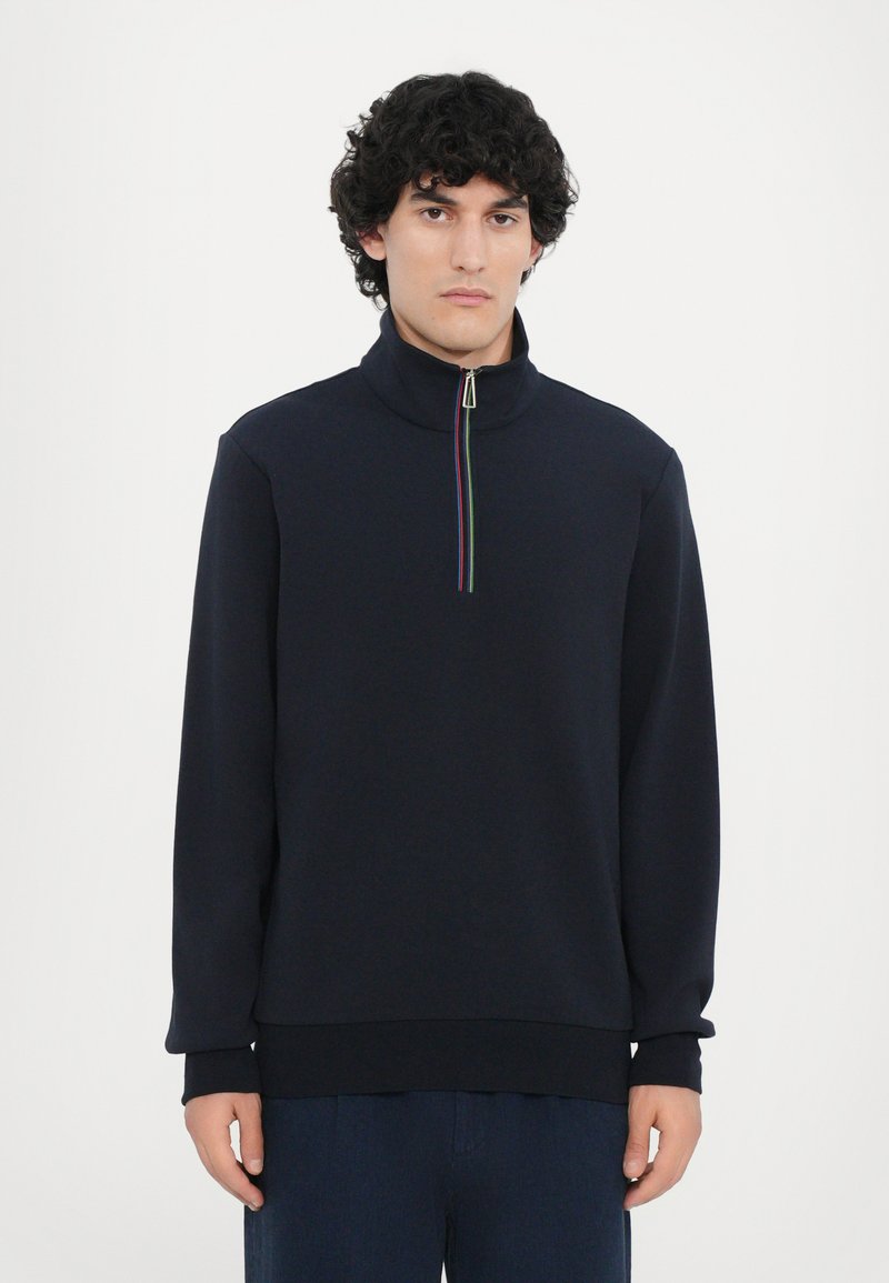 Suéter azul marino con cuello alto, cremallera cuartilla y un acento de rayas multicolores. Fabricado en un material suave y texturizado, de corte relajado.