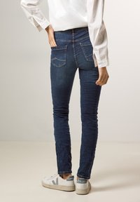 Jeans skinny en denim bleu foncé, avec une taille haute, des poches arrière avec un motif de couture simple et une légère texture usée.