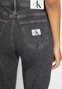 Černé džíny z denimu s mírně vybledlým vzhledem, s dvěma zadními kapsami a bílou cedulkou s logem Calvin Klein Jeans.