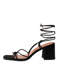 Sandalo con tacco in suede nero con punta quadrata, cinturini incrociati alla caviglia e tacco a blocco spesso. Presenta una fodera interna liscia.