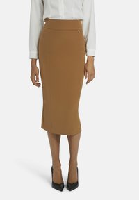 Jupe crayon marron en tissu extensible, avec une taille haute et une coupe ajustée, associée à des escarpins noirs à bout pointu.