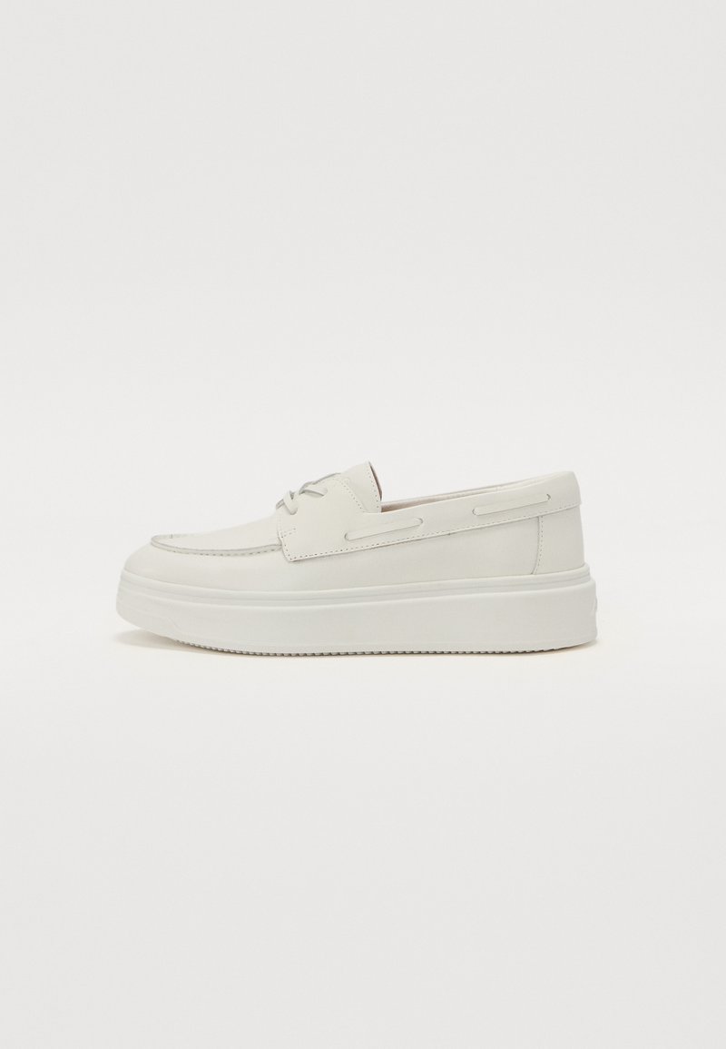 Hvite lær slip-on sko med rund tå, minimal søm, og tykk hvit gummisåle. Har sideakenter for snøring.