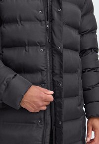 Chaqueta de plumas negra con un diseño acolchado y con forma de rombos. Cierre frontal con cremallera y botones a presión, y puños acanalados para mayor calidez.