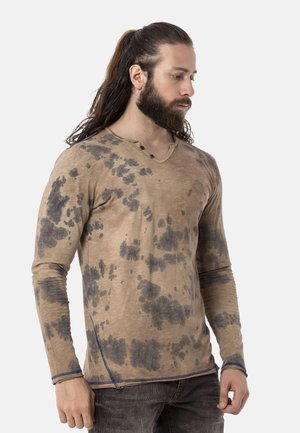 Beige langwerpige T-shirt met zwart spetterpatroon, V-hals en blauwe stikselaccenten. Gemaakt van lichtgewicht stof met een gestructureerde afwerking.