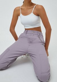 Un pantalon cargo lilas présente des poches avant, un accent de chaîne et une fermeture à bouton. Associé à un top court blanc ajusté, cela met en avant un look décontracté.