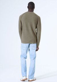 Olivgrünes Langarmshirt mit runder Ausschnitt, kombiniert mit hellblauen Jeans und beigen Sandalen, von hinten betrachtet.