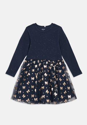 Marineblaues Langarmkleid mit glitzernden Punkten oben und einem Rock mit transparenter Überlagerung und metallisch goldenen Schleifenmustern.