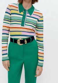 Multicolore gestreepte gebreide polo met een groene kraag en knoopsluiting, gecombineerd met hoge groene broek en een zwarte riem.