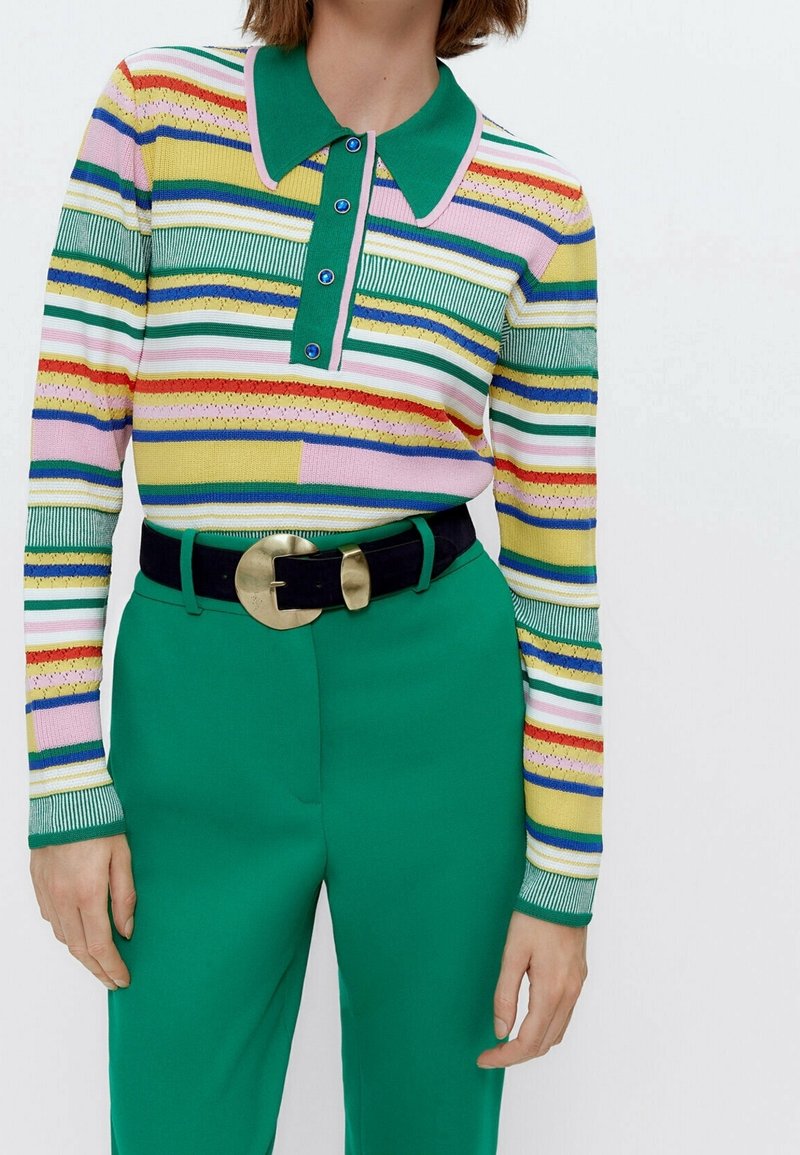 Multicolore gestreepte gebreide polo met een groene kraag en knoopsluiting, gecombineerd met hoge groene broek en een zwarte riem.