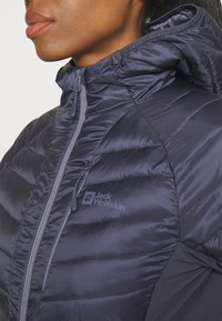 Gevoerde, marineblauwe jas met een hoge kraag, rits en logo-detail. Beschikt over een gestructureerd oppervlak en horizontale naden voor isolatie.