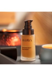 AHAVA Time to Revitalize Extreme Night Treatment-serumflaske med sort pumpe på træbord, varmt glødende baggrundslys.