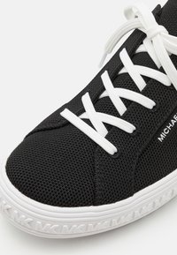 Baskets en mesh noir avec lacets blancs, semelle blanche embossée du logo "MK" et marquage "MICHAEL" sur le côté.