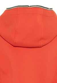 Nahaufnahme eines leuchtend orangefarbenen Hoodies, der die Rückseite der Kapuze zeigt, mit sichtbaren Nähten und einem schwarz-weißen gestreiften Saum entlang des Halsausschnitts.