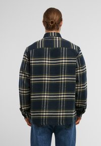 Granatowa flanelowa koszula w kratę z kremowymi i zielonymi paskami, z ostro zakończonym kołnierzykiem i długimi rękawami, ozdobnym przeszyciem oraz zaokrąglonym hemem.