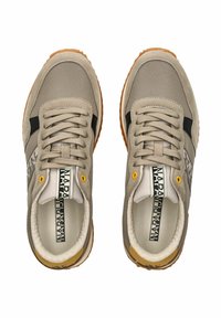 Zapatillas deportivas beige con una parte superior de tela texturizada, acentos laterales negros, ojales amarillos y una suela de goma con un patrón de relieve.