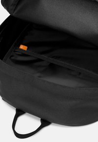 Svart ryggsäck med slät yta, har ett dragkedjestängd topp och en orange etikett inuti. Inkluderar två sidofickor för enkel bärande.