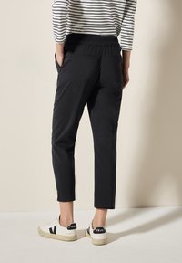 Zwarte tapered broeken met een elastische tailleband, met zijzakken, gecombineerd met witte sneakers met zwarte accenten en een gestreepte top.