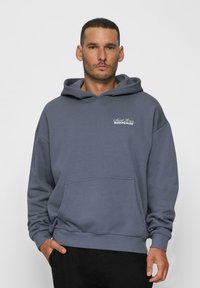 Felpa grigia con tasca a marsupio, cappuccio con coulisse e dettaglio del logo sul petto. Realizzata in un tessuto morbido e testurizzato. Vestibilità comoda.