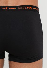 Mustat puuvillaboxerit joustavan vyötärönauhalla, jossa on kontrastivärinen oranssi brändinimi "DIM". Liukas rakenne, istuva muotoilu.