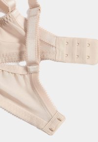 Soutien-gorge en tulle beige avec bretelles réglables et fermeture à crochets et œillets comportant trois rangées pour un ajustement de taille.