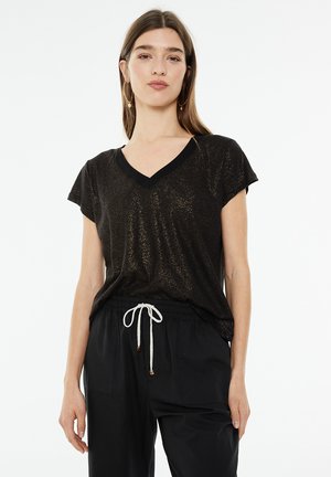 Camiseta negra de cuello en V con mangas cortas, que presenta una sutil textura brillante. Combinada con pantalones negros holgados y un detalle de cordón.