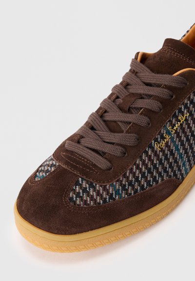Brūni zamšādas sporta apavi ar rakstainiem auduma paneļiem, brūnām auklām, gumijas zoli un zelta "Paul Smith" logo sānos.