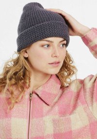 Gorro de lana gris trenzado con banda texturizada y parte superior cónica, combinado con una chaqueta a cuadros en tonos rosa y crema que cuenta con cierre delantero y cuello.