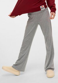 Szare spodnie dzwony o miękkiej fakturze, z elastycznym paskiem w talii. Noszone z beżowymi butami wsuwanymi i bordowym topem z naszywką z logo.