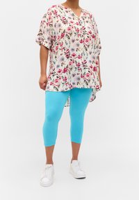Květinová tunika s růžovými a modrými květy na krémovém pozadí, v kombinaci s jasně modrými legínami a bílými teniskami. Příliš velké, krátké rukávy.