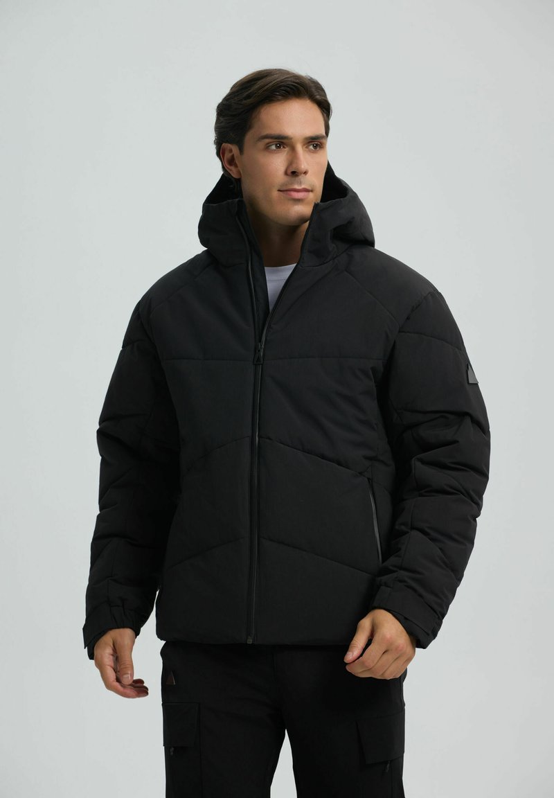 Giacca a vento nera con cappuccio, caratterizzata da un design trapuntato, maniche lunghe e tasche anteriori con zip. Texture liscia e materiale leggero.