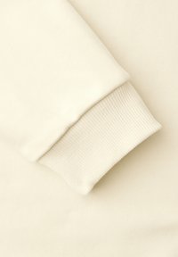 Manga de sudadera color crema con puño acanalado, mostrando la textura de la tela y detalles de costura.