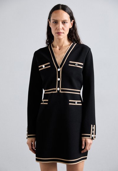 Rochie neagră cu mâneci lungi, decolteu în V, cu dungi crem și butoane rotunde argintii pe buzunare și manșete. Țesătură fină cu un design structurat.