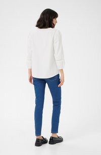 White blouse with puffed sleeves and lace detailing, paired with blue skinny jeans and black loafers, viewed from behind.