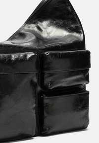 Czarna skórzana torba o teksturowanym wykończeniu, z wieloma kieszeniami, gładkim zapięciem na zamek oraz charakterystycznym trójkątnym kształtem.