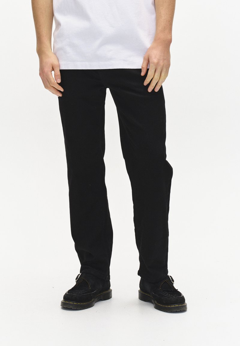 Pantalon noir en tissu doux, design à jambes droites, porté avec des chaussures sombres, associé à un t-shirt blanc uni, avec un minimum de détails.