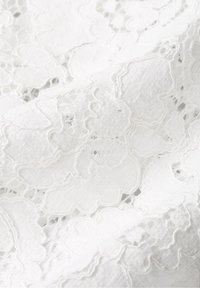 Tissu en dentelle blanche avec un motif fleuri, présentant des découpes intriquées et une surface texturée, tombant doucement avec une apparence délicate.