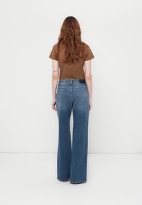 Jean en denim à jambe large dans un délavage moyen avec une légère décoloration. Fini avec une pièce en bleu foncé à l'arrière et deux poches arrière.