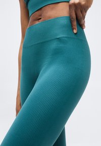 Κοντινό πλάνο ενός ατόμου που φοράει ριμπ μαρινό κολάν γυμναστικής και ταιριαστό crop top, με το ένα χέρι να ρυθμίζει τη μέση.