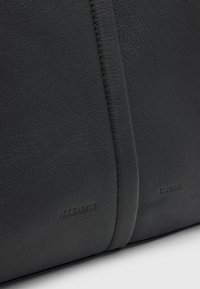 Sac en cuir noir avec une finition texturée, avec des coutures visibles et une marque en relief "ALLSAINTS" et "LONDON" sur les côtés.