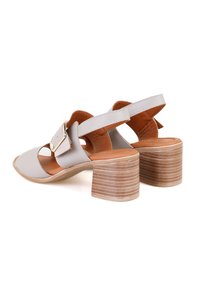 Sandales en cuir gris avec un bout ouvert, un design découpé et une large sangle avec une boucle. Talon en bois épais avec des rainures horizontales.
