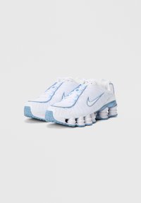 Nike-sneakers har en hvit syntetisk overdel med lyseblå detaljer og et særpreget såledesign. Teksturert stoff og snøring.